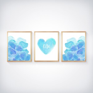 May include: Three framed watercolor prints with a blue and purple color scheme. The center print features a heart shape with the name "Ella" written inside. The prints are perfect for a nursery or child's room.