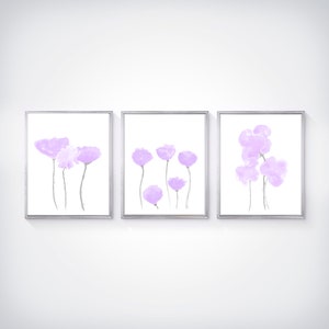 Pu&ograve; includere: Set di tre stampe incorniciate con dipinti astratti ad acquerello di fiori viola. Le stampe sono in semplici cornici argentate e hanno uno sfondo bianco.