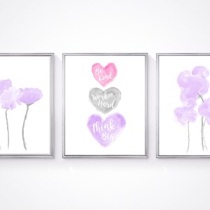 May include: Three watercolor prints with a white background. The center print features three hearts with the words "Be Kind", "Work Hard", and "Think Big" written in white. The left and right prints feature purple watercolor flowers.