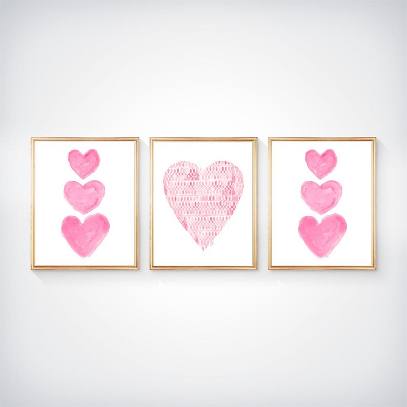 K&ouml;nnte beinhalten: Ein Set aus drei gerahmten Wandbildern. Die linken und rechten Bilder zeigen jeweils eine vertikale Anordnung von drei rosa Aquarellherzen. Das mittlere Bild zeigt ein gro&szlig;es Herz mit einem sich wiederholenden rosa-wei&szlig;en Muster.