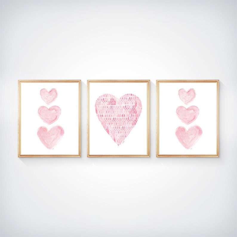K&ouml;nnte beinhalten: Ein Set aus drei gerahmten Wandbildern mit rosa Herzillustrationen. Die beiden &auml;u&szlig;eren Rahmen zeigen drei &uuml;bereinander angeordnete Herzen im Aquarellstil, w&auml;hrend das mittlere Bild ein gro&szlig;es Herz mit texturiertem Muster zeigt.