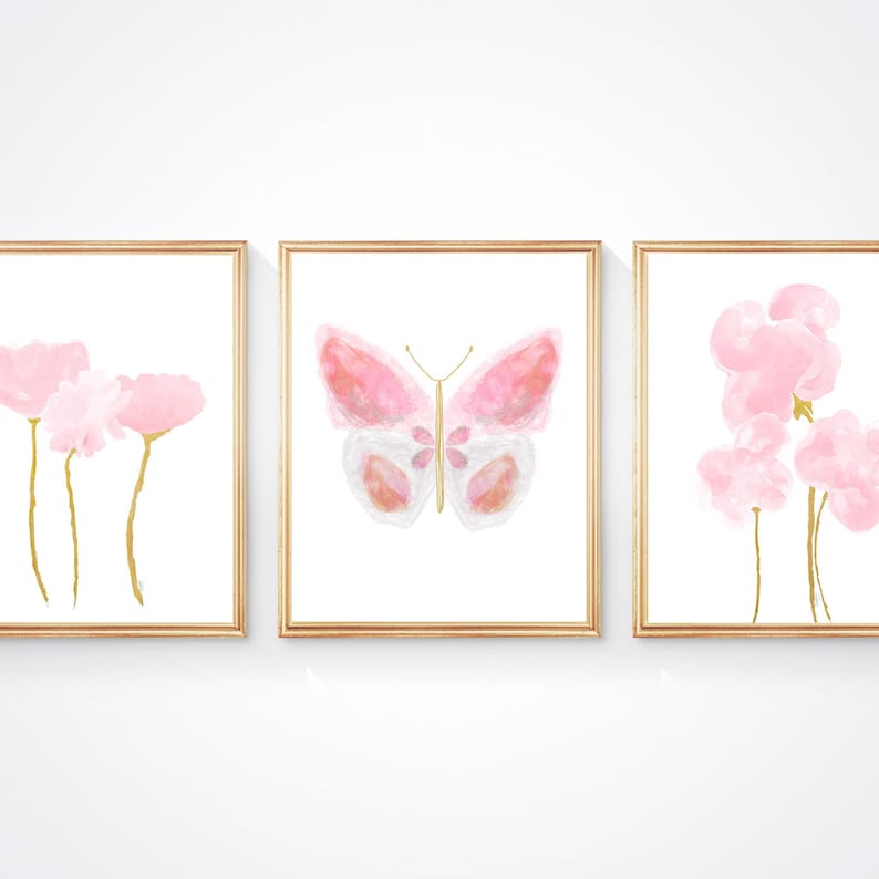 Three unframed watercolor prints with a pink and gold color scheme. The center painting features a pink butterfly with gold accents. The paintings on either side feature pink flowers with gold stems.