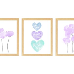 May include: Three framed watercolor prints with a light wood frame. The center print features three watercolor hearts stacked vertically with the words "Be Kind", "Work Hard", and "Think Big" written in white. The left and right prints feature watercolor flowers in shades of purple.