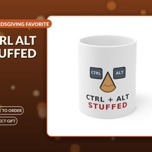 Puede incluir: Una taza de cerámica blanca con un gráfico de dos teclas de computadora gris oscuro etiquetadas como CTRL y ALT, con una forma triangular marrón que se asemeja a un alimento relleno entre ellas. Debajo del gráfico, el texto dice CTRL + ALT STUFFED.