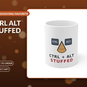 Peut inclure: Un mug en céramique blanc orné d'un graphique représentant deux touches d'ordinateur gris foncé étiquetées CTRL et ALT, avec un personnage triangulaire beige souriant au centre. Le texte CTRL + ALT STUFFED est inscrit en noir et rouge.