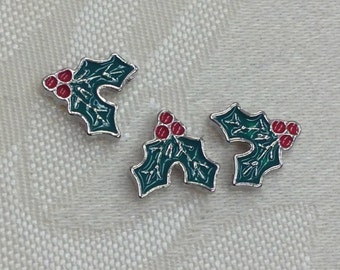 May include: Three silver charms shaped like holly leaves with red berries. The charms are green and red with a silver outline.
