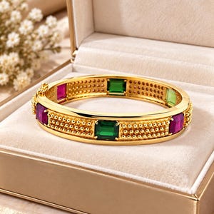 Puede incluir: Una pulsera rígida articulada de tono dorado con una superficie texturizada de cuentas y gemas rectangulares alternas en tonos vibrantes de verde esmeralda, rojo rubí y verde lima claro, asegurada con un cierre lateral.