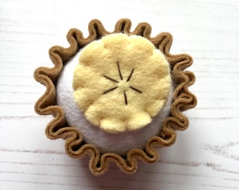 Può includere: Una torta di feltro con una crosta marrone e un ripieno di feltro giallo. La torta è un giocattolo fatto a mano.