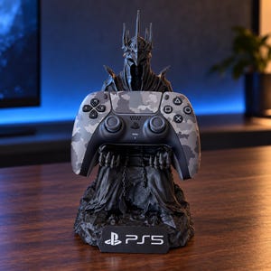 May include: A black figurine of a spiked, armored knight holding a gray and white camouflage gaming controller. The base features a black rectangular plaque with the white PlayStation logo and the text PS5 printed in a clean, sans-serif font.