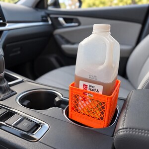 May include: A bright orange plastic miniature crate designed to fit into a vehicle cup holder. The crate holds a translucent plastic jug filled with a light brown liquid, featuring a white label with the text Diet Half & Half visible.