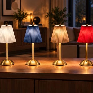 Peut inclure: Quatre lampes de table avec des bases et des tiges en métal doré, chacune dotée d'un abat-jour en tissu plissé. Les abat-jours sont blancs, bleus, beiges et rouges. Chaque lampe possède une base circulaire et une tige verticale fine.