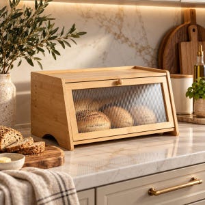 May include: A rectangular bamboo bread box with a slanted front and a clear, vertically ribbed glass door. The door features a small wooden knob for opening. Inside the box, three round loaves of bread are visible through the textured glass.
