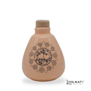 May include: A peach-colored ceramic bottle with a rounded body and a light brown wooden stopper. The front features a black line-art design of a sunburst with floral petals and two central hearts surrounded by swirling patterns.
