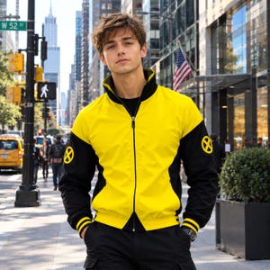 May include: A yellow and black zip-up jacket featuring a high collar and a circular yellow X-Men logo on each sleeve. The jacket has a central black zipper, black sleeves with yellow striped cuffs, and a solid yellow front and back panel.