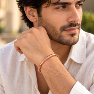 Peut inclure: Un bracelet manchette en métal de couleur cuivre, lisse et poli, avec un profil arrondi. Le bracelet présente un design en anneau solide et continu qui entoure le poignet, mettant en valeur une finition métallique chaude et réfléchissante.