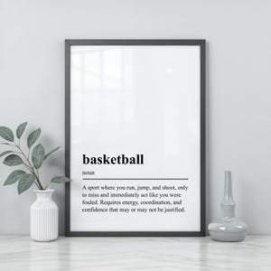 May include: A black framed wall art print featuring a dictionary-style definition of the word basketball. The text reads: basketball, noun, A sport where you run, jump, and shoot, only to miss and immediately act like you were fouled.