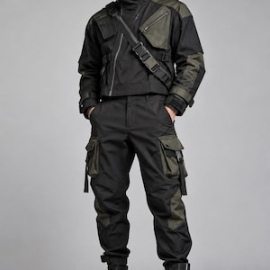 Può includere: Una giacca tattica nera e verde oliva con collo alto, cerniera diagonale e tasche multiple, abbinata a pantaloni cargo neri e verde oliva coordinati con tasche laterali dotate di cinghie e stivali da combattimento neri stringati.