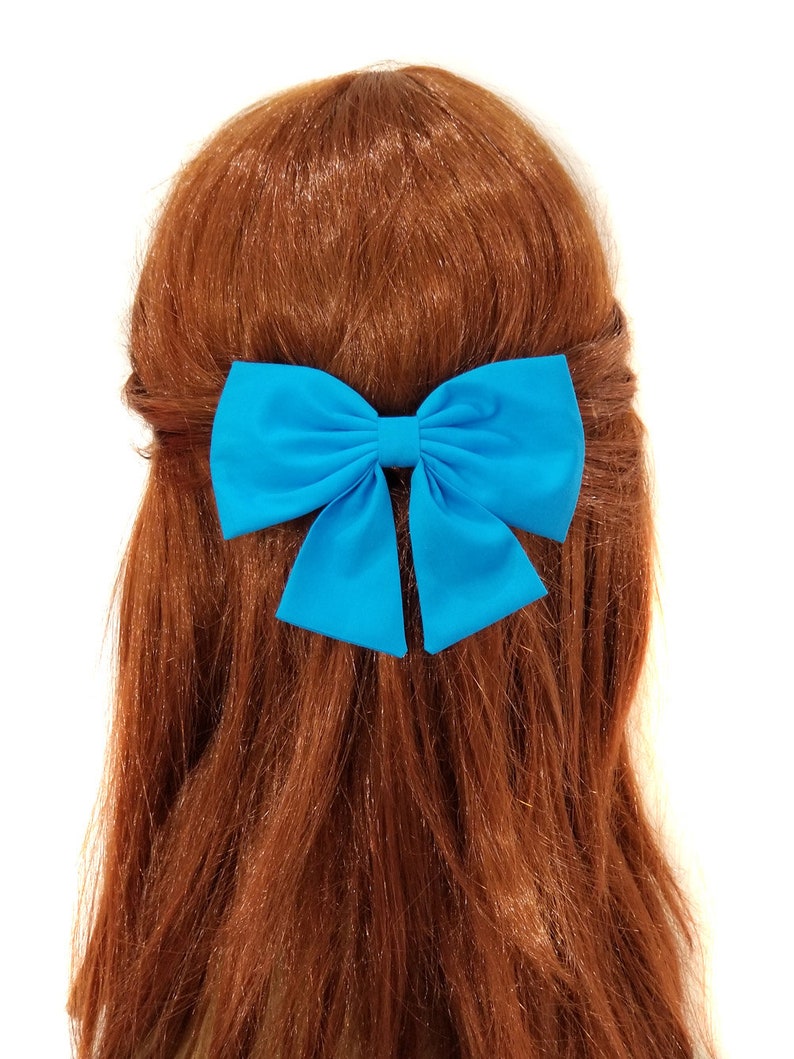 May include: A bright blue bow hair clip. The bow is made of a soft, satin-like fabric and is tied in a classic bow shape.