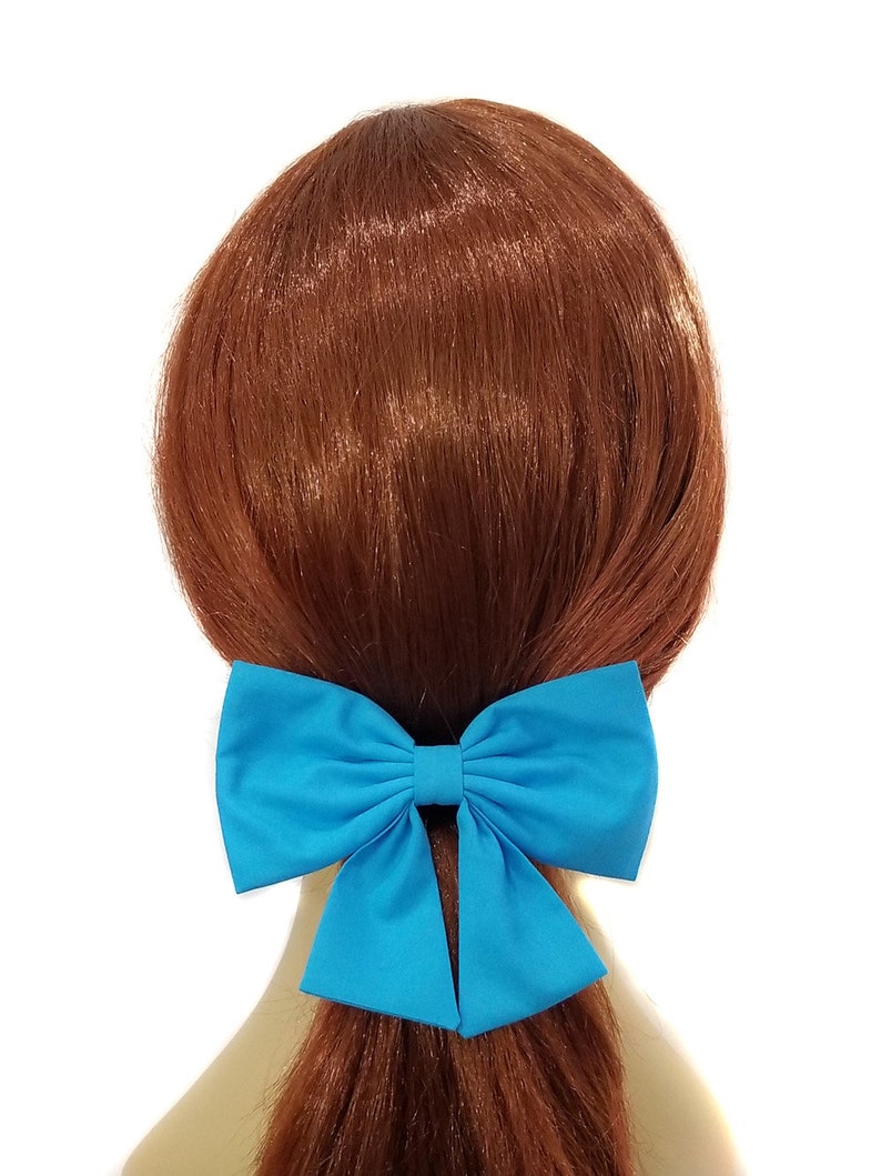 May include: A large turquoise blue fabric bow hair clip. The bow is tied in a large, full loop with two tails.
