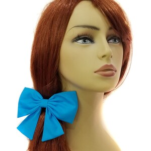 May include: A bright turquoise fabric bow hair tie. The bow is tied in a large, full loop with two tails.