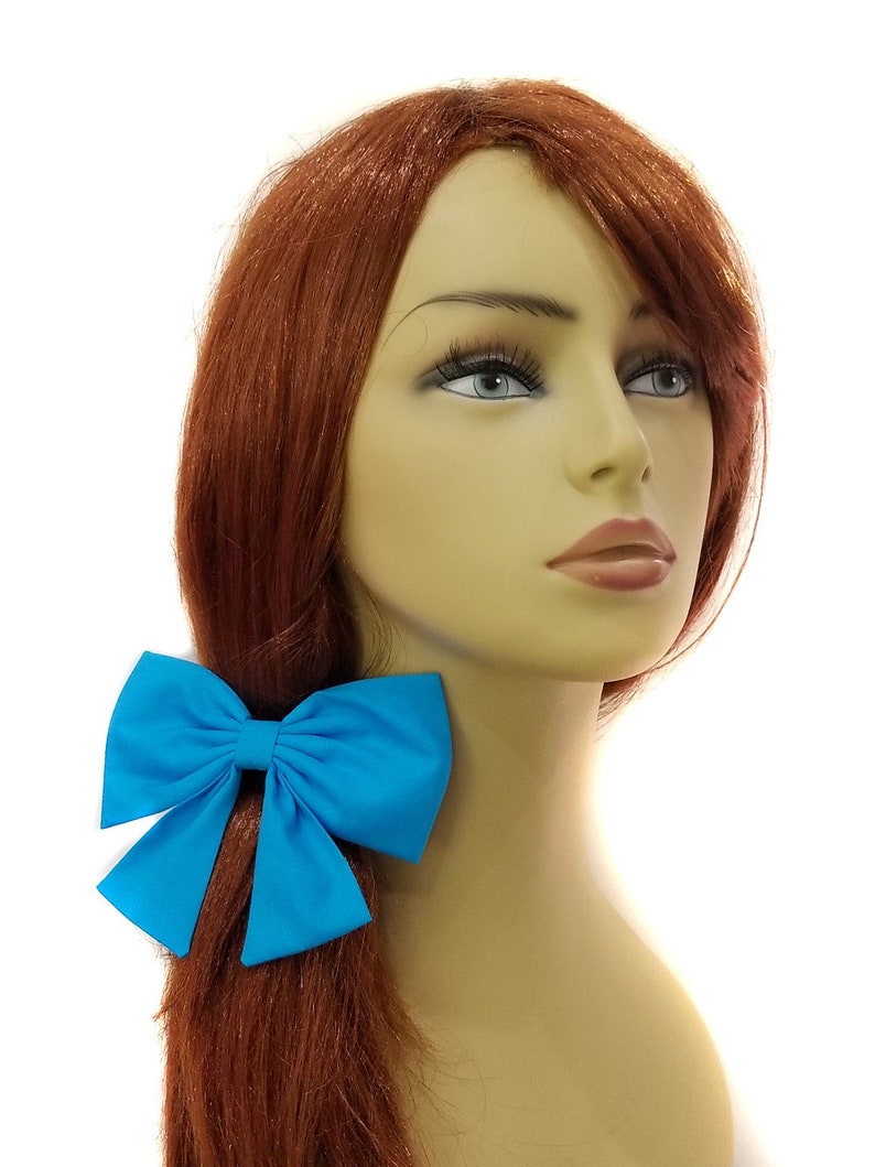 May include: A bright turquoise fabric bow hair tie. The bow is tied in a large, full loop with two tails.