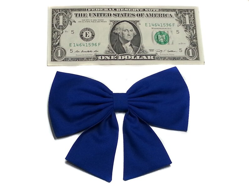 May include: A large, royal blue bow made of fabric. The bow is tied in a classic style with two loops and a center knot.