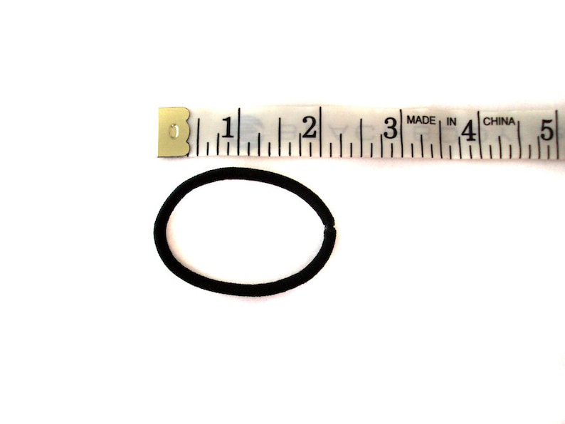 May include: A black hair elastic measuring approximately 2 inches in diameter, next to a white tape measure marked with inches.