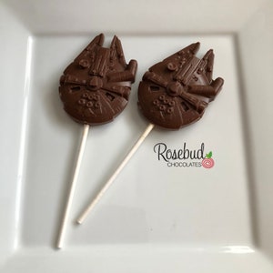 May include: Two chocolate lollipops shaped like the Millennium Falcon from Star Wars. The lollipops are on a white plate with the text "Rosebud Chocolates" printed on the plate.