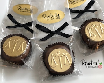 May include: Three clear cellophane bags with black ribbon bows, each containing a chocolate favor with a gold scale of justice design. The bags have a gold oval sticker with the text "Rosebud Chocolates" on them.