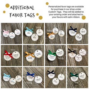 May include: Assortment of round, white, paper favor tags with black text and various designs. The tags are tied with satin ribbon in different colors, including red, blue, green, and gold. The tags feature text such as "Cheers to 50 Years", "Happy Birthday", "Thank You", and "It's a Boy".