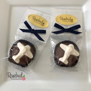 May include: Two clear cellophane bags with navy blue ribbon bows, each containing a chocolate favor with a white airplane design. The bags have a gold oval sticker with the text "Rosebud Chocolates".
