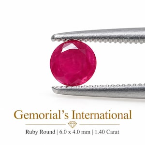 May include: A round, faceted, vibrant red ruby held by silver-toned metal tweezers. Below the gemstone, the text reads: Gemorial's International, Ruby Round | 6.0 x 4.0 mm | 1.40 Carat. The ruby displays a clear, brilliant cut with deep red hues.