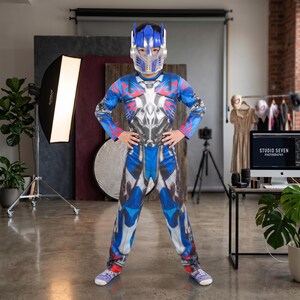 Può includere: Un costume integrale con un design da personaggio robotico blu, argento e rosso, completo di casco in plastica abbinato. La tuta a maniche lunghe presenta dettagli meccanici stampati, inclusi motivi a fiamma sulle spalle e sul petto.