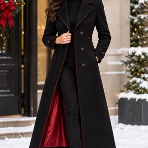 May include: A long black coat featuring a deep red lining, a notched collar with red piping, and double-breasted buttons. The coat includes long sleeves with buttoned cuffs, a fitted waist, and a full-length hemline, worn over a black turtleneck.