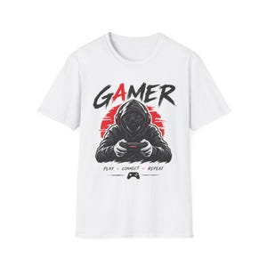 Könnte beinhalten: Ein weißes Kurzarm-T-Shirt mit einer Grafik einer Kapuzenfigur, die Kopfhörer trägt und einen Gamecontroller vor einer roten Sonne hält. Der Text GAMER steht darüber, darunter die Wörter PLAY CONNECT REPEAT und ein Controller-Symbol.