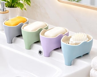 以下が含まれることがあります： グレー、ライトグリーン、ラベンダー、ライトブルーのプラスチック製ソープディッシュ4点。3つのディッシュには黄色と白の長方形の石鹸が置かれ、ライトブルーのディッシュには柔らかい毛の小さな丸い白いスクラブブラシが入っています。