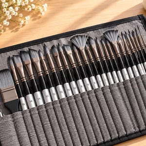 Könnte beinhalten: Ein Set aus Künstlerpinseln und einem Malmesser, angeordnet in einer grauen Stofftasche zum Aufrollen. Die Pinsel haben schwarze Griffe mit silbernen Zwingen und grauen Synthetikborsten, wobei verschiedene Größen auf den Zwingen aufgedruckt sind.