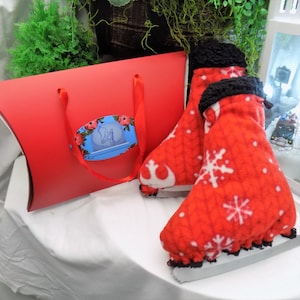 Könnte beinhalten: Rote und weiße Fleece-Schlittschuhüberzüge mit Schneeflockenmuster und schwarzem Besatz. Die Überzüge sind in einer roten Geschenkbox mit blau-weißem Logo verpackt.