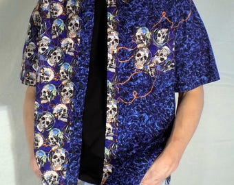 May include: A blue short-sleeved button-down shirt with a skull and headphone print. The shirt has a blue and orange pattern on one side and a skull print on the other side.