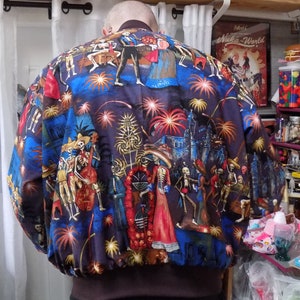 May include: A blue bomber jacket with a colorful print of skeletons celebrating with fireworks. The print features a castle, flowers, and a variety of other details.