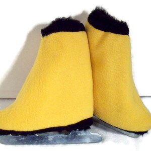 Puede incluir: Un par de patines de hielo con cubiertas de color amarillo brillante y ribete negro. Las cuchillas son plateadas y las cubiertas tienen una textura suave y difusa. Patines para patinaje recreativo.