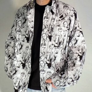 May include: A white button-down shirt with a black and white print of characters from the Harry Potter series. The shirt has a long sleeve and a collared neckline.