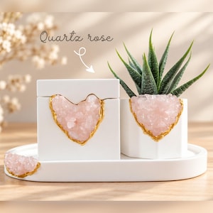 Peut inclure: Une boîte rectangulaire blanche, un pot hexagonal blanc contenant une plante succulente verte et un petit plateau blanc, tous ornés de cristaux de quartz rose incrustés avec des bords dorés. Le texte Quartz rose est visible au-dessus.