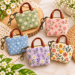 May include: Five miniature tote bag keychains featuring various fabric patterns including green, pink, blue, purple, and cream floral and polka dot prints. Each bag has brown handles, a metal zip, a snap button closure, and a metal lobster clasp.