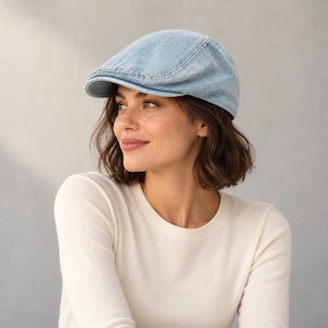 May include: A light blue denim flat cap featuring a structured crown, a short stiff brim, and visible stitched seams along the panels. The fabric has a faded wash appearance with a textured surface, providing a classic silhouette for headwear.