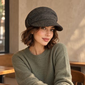 May include: A dark gray and black houndstooth patterned newsboy cap with a structured crown and a short, stiff brim. The cap features a textured, woven fabric construction with a rounded silhouette that sits firmly on the head.