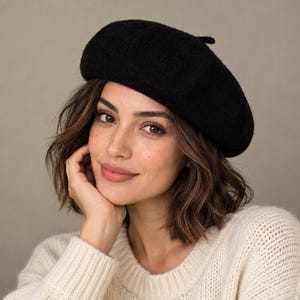 May include: A solid black beret with a soft, felted texture and a small, rounded top detail. The hat features a classic circular shape that sits comfortably on the head, providing a clean, uniform appearance with no additional patterns or embellishments.