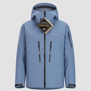 May include: A light blue hooded jacket featuring a full-length black front zipper, two vertical chest pockets with black zippers, and a small black zipper pocket on the left sleeve. A Gore-Tex tag hangs from the collar, and the Arc'teryx logo is visible.