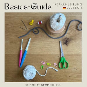Könnte beinhalten: Ein Basics-Guide PDF-ANLEITUNG DEUTSCH mit zwei Knäueln weißem Garn, eines auf einem Holzständer, zwei Häkelnadeln mit pinken und blauen Griffen, einer Schere mit grünen Griffen, zwei Nähnadeln, einem gelben Werkzeug und vier Maschenmarkierern.