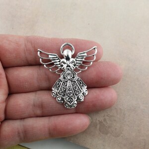 Pu&ograve; includere: Ciondolo angelo in argento con dettagli intricati e un'aureola. L'angelo ha le ali e un abito fluido.